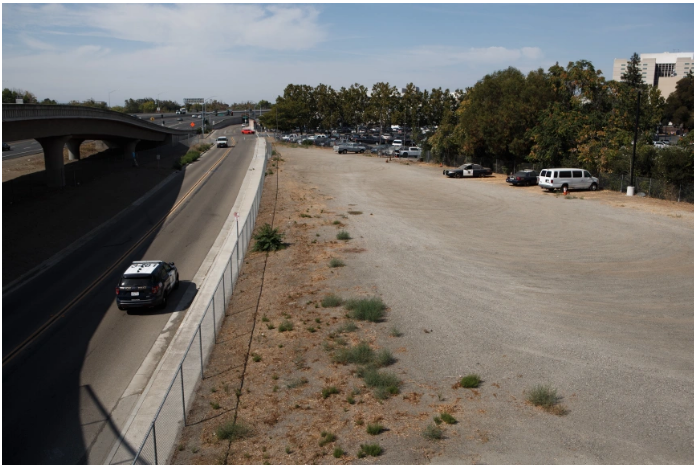 Site for interim housing, in an unpaved parking lot against a freeway onramp